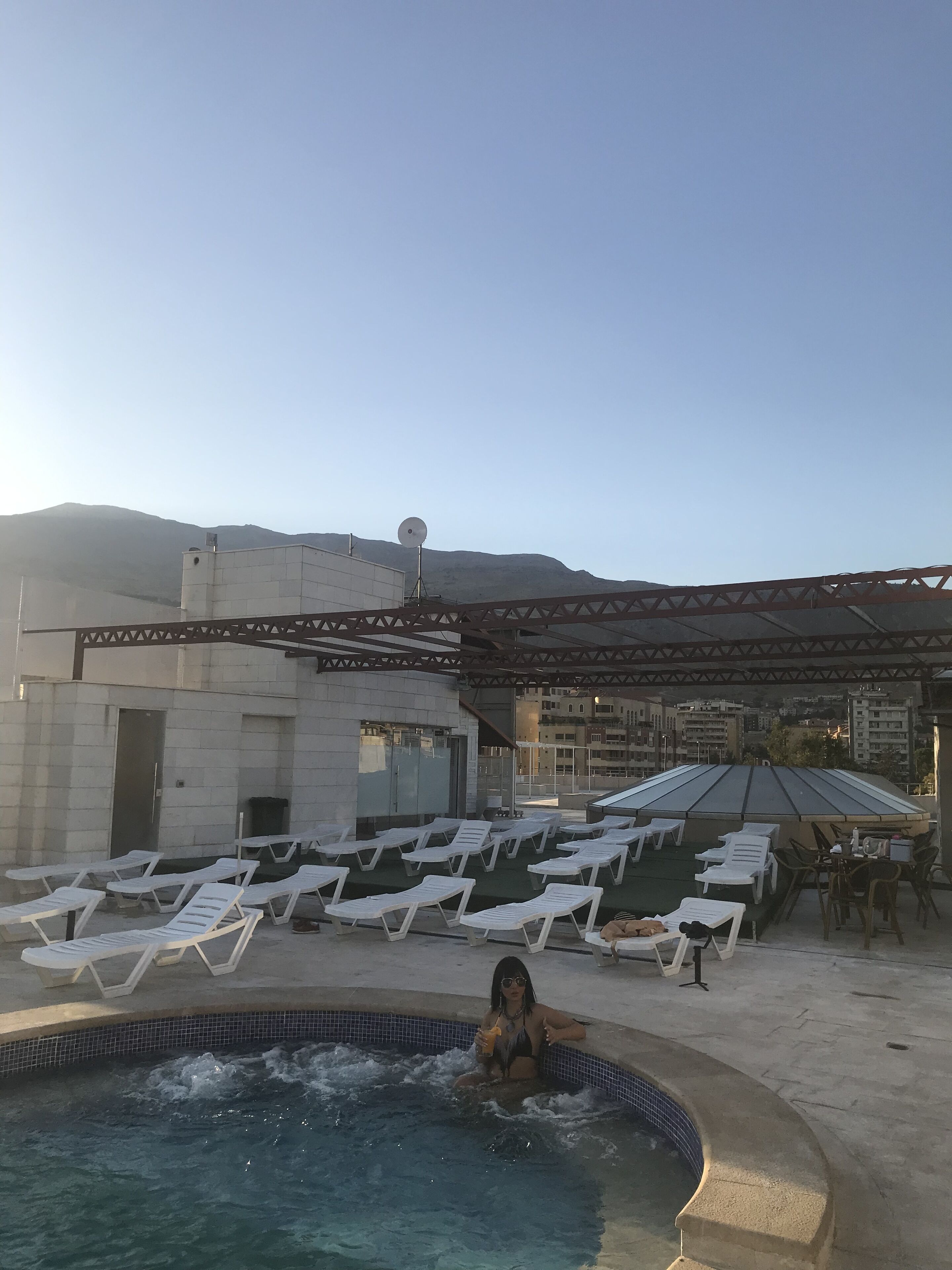 A rooftop pool area with lounge chairs and a person in the pool.