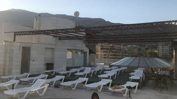 A rooftop pool area with lounge chairs and a person in the pool.