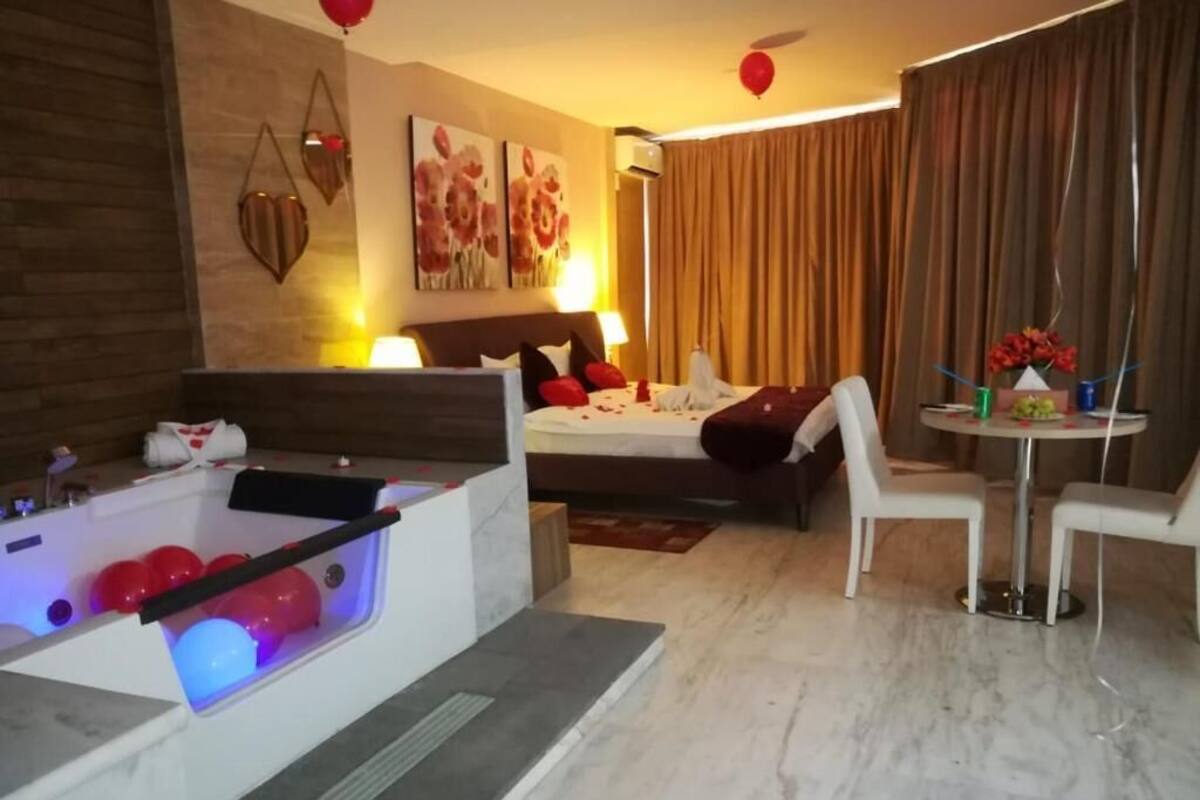 Une chambre d’hôtel moderne dotée d’un bain à remous, d’un lit avec des oreillers rouges, d’une petite table à manger et d’une grande fenêtre avec des rideaux.