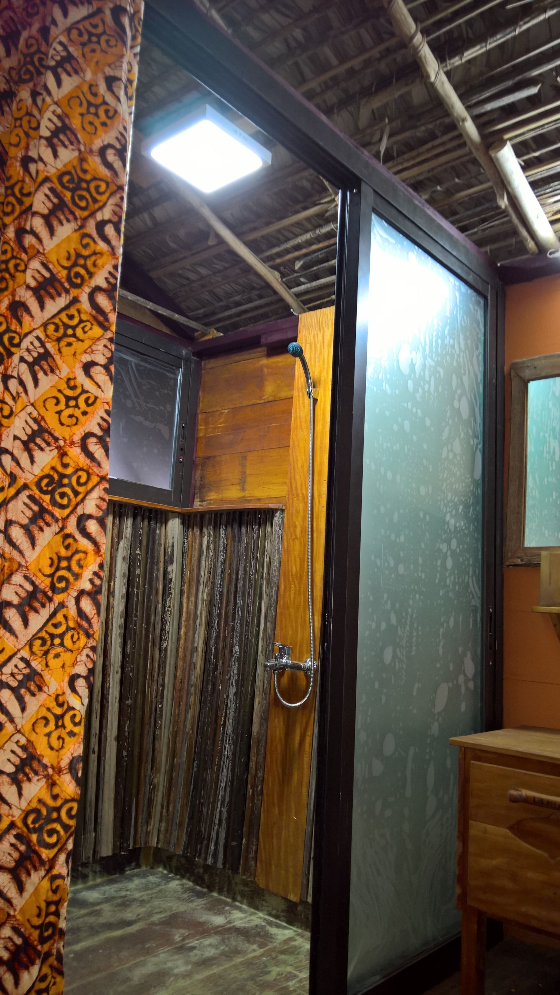 Ein Badezimmer mit Dusche, Holzvertäfelung, einem Spiegel und einem gemusterten Vorhang.