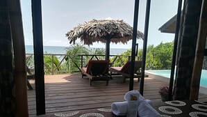 A wooden deck with lounge chairs and a thatched umbrella overlooking a pool and ocean. - Libassa Ecolodge (Marshall)