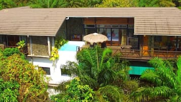 Una villa moderna con una amplia piscina exterior, rodeada de exuberante vegetación tropical.