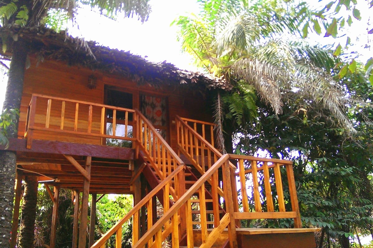 A wooden cabin with a balcony and staircase, surrounded by trees.