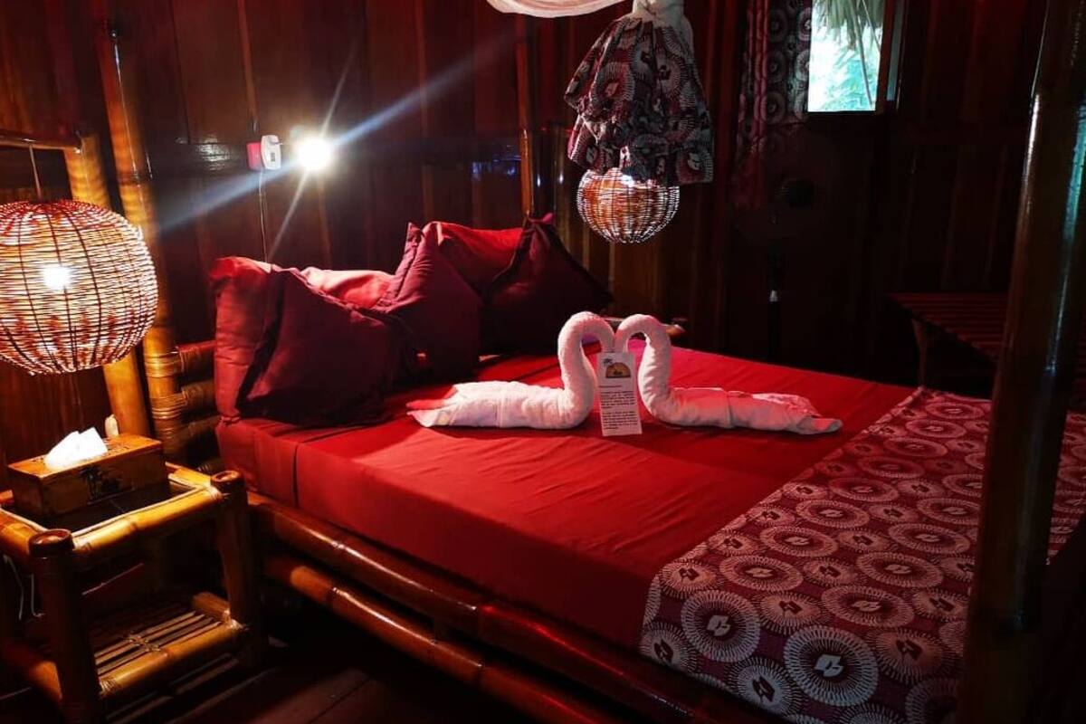 A neatly made bed with red bedding, a wooden headboard, and a patterned throw.