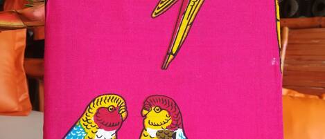A vibrant pink fabric with a colorful bird design, likely a decorative item or artwork.