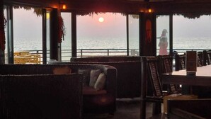 An indoor seating area with a view of the ocean at sunset, featuring wicker furniture and a wooden table. - Libassa Ecolodge (Marshall)