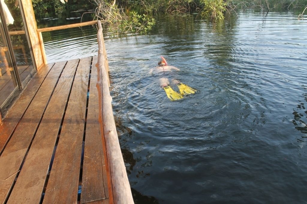A wooden deck extending over a body of water with a person swimming.