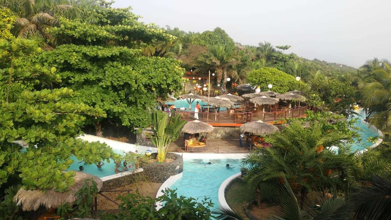 Et resort med flere swimmingpools omgivet af frodig vegetation og stråtækte bygninger.