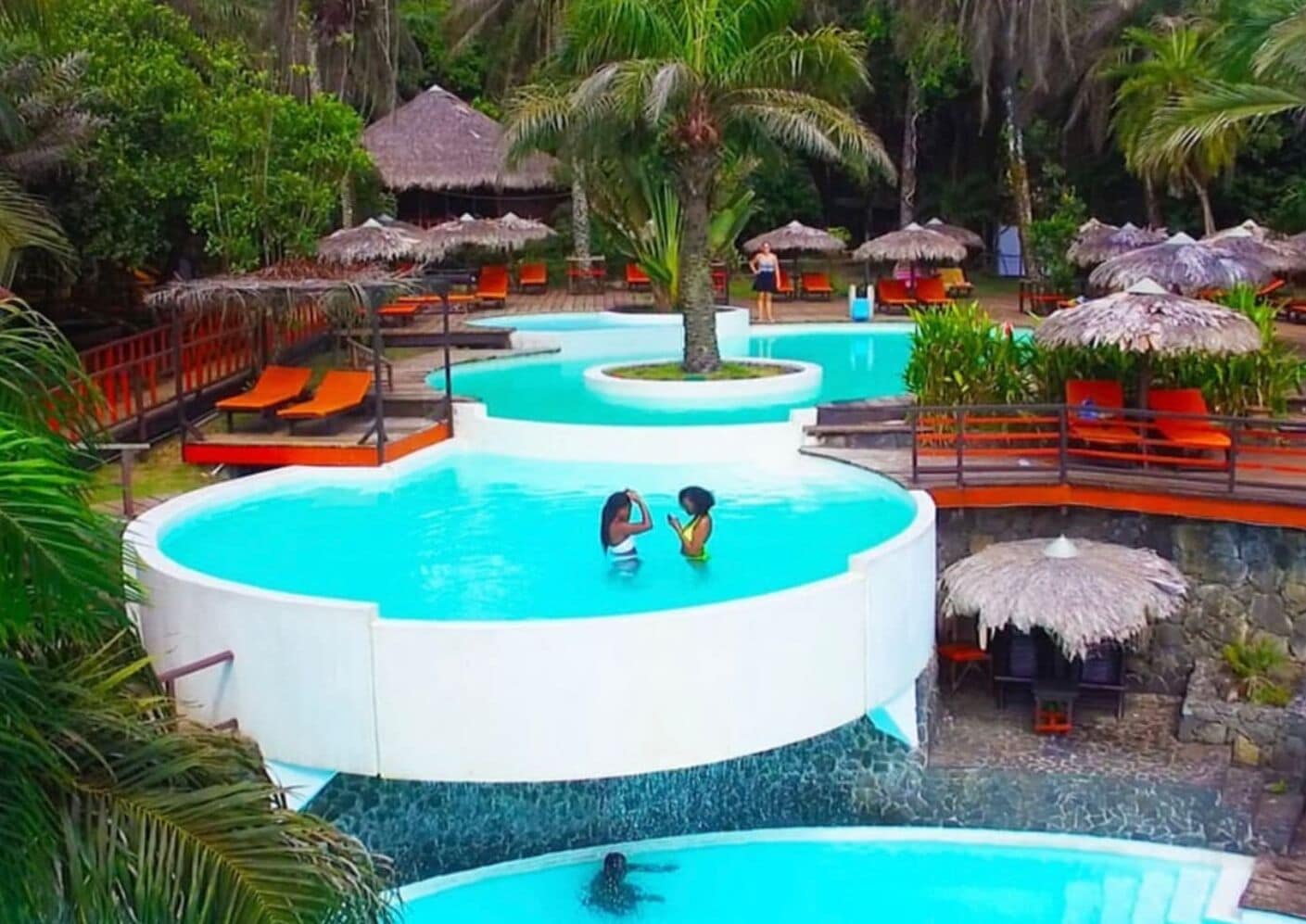 A resort with multiple swimming pools, palm trees, and thatched umbrellas.