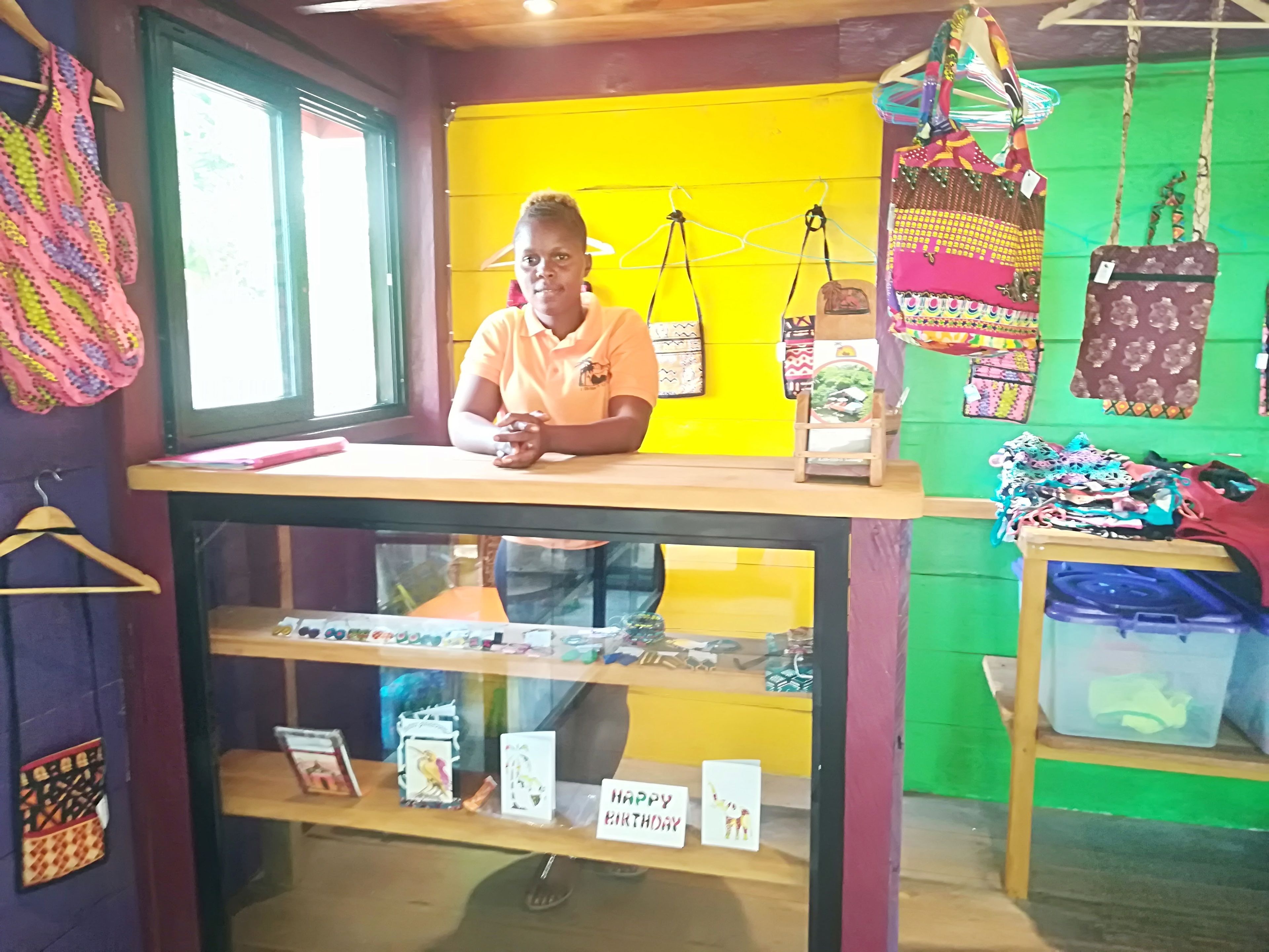 Una tienda con un muro amarillo, varias bolsas exhibidas y una persona sentada en un mostrador.