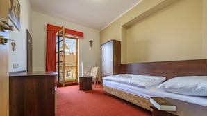 A hotel room with a bed, a desk, a chair, a wardrobe, and a view of a building through a window.