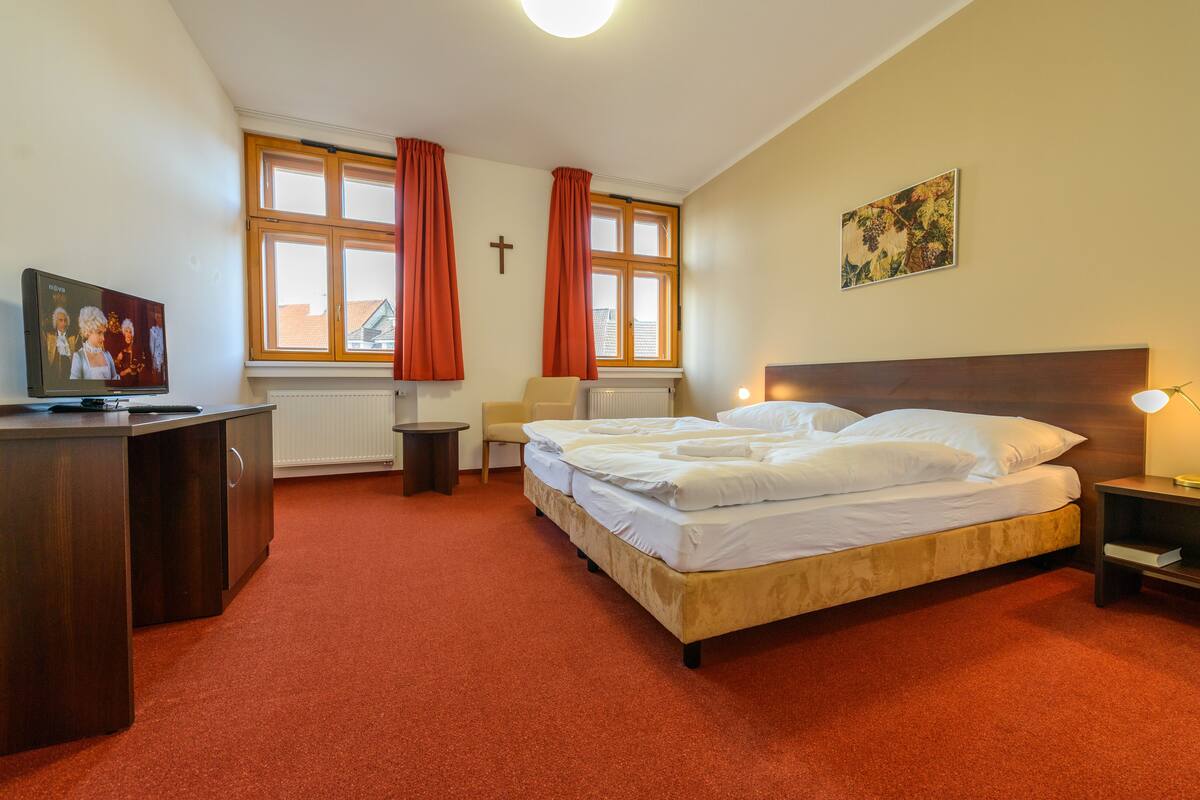 Ein Hotelzimmer mit einem Bett, einem Schreibtisch, einem Sessel, einem Fernseher und einem Fenster mit Vorhängen.
