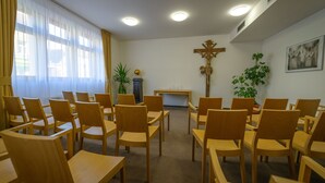 A church interior with wooden pews arranged in rows, a wooden crucifix on the wall, and a small altar with candles.