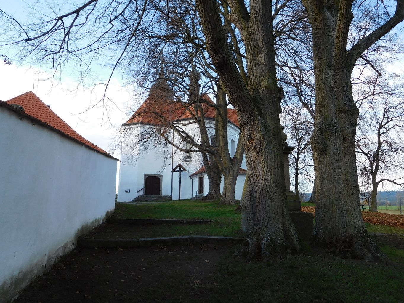 A white building with a red roof, surrounded by trees and a grassy area.
