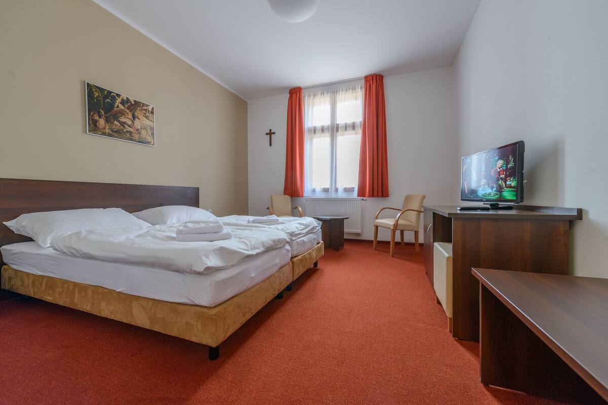 Ein Hotelzimmer mit Bett, Schreibtisch, Stuhl, Fernseher und einem fenster mit Vorhängen.