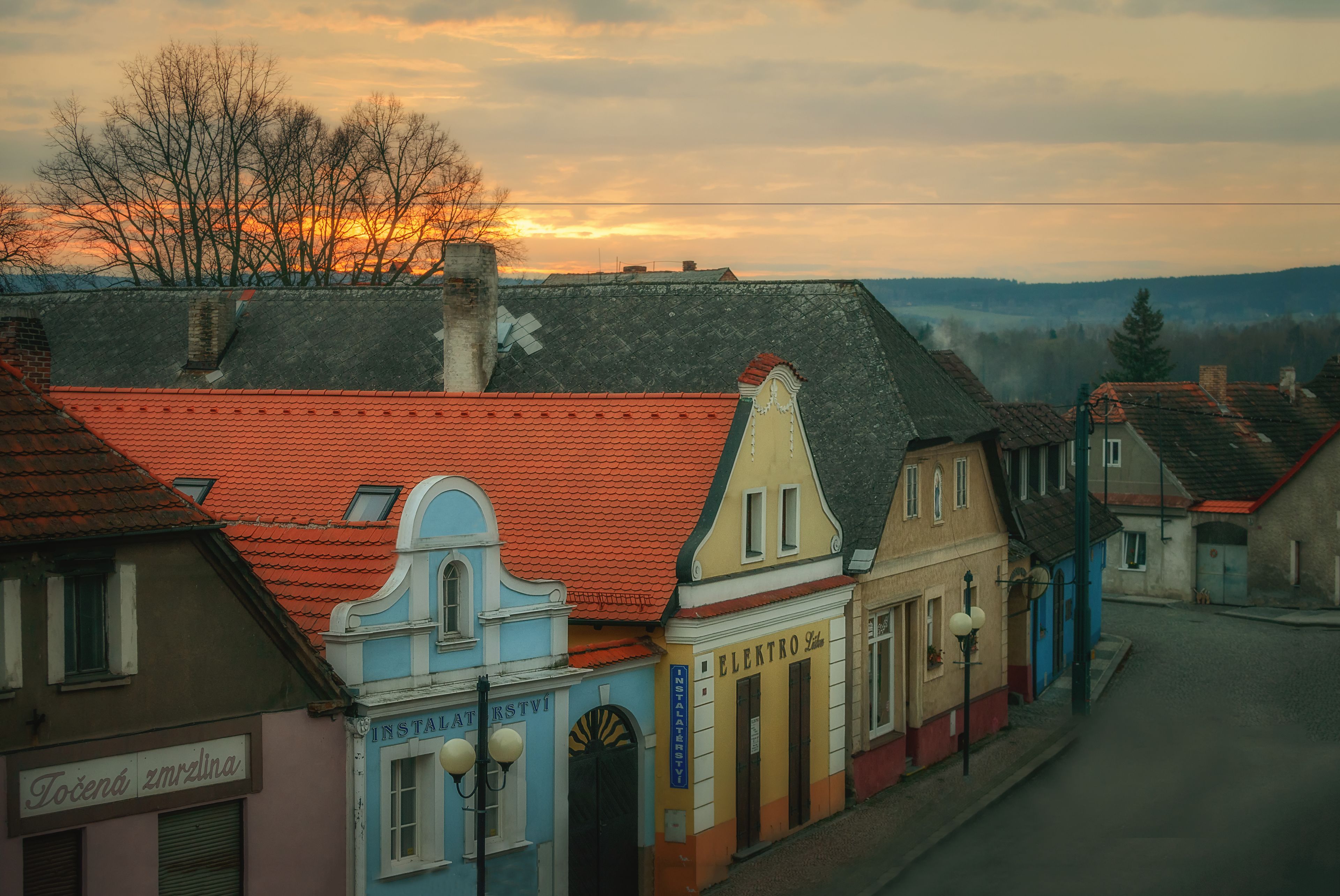 Une vue d’une rue d’une ville, avec des bâtiments à l’architecture traditionnelle et un coucher de soleil en arrière-plan.
