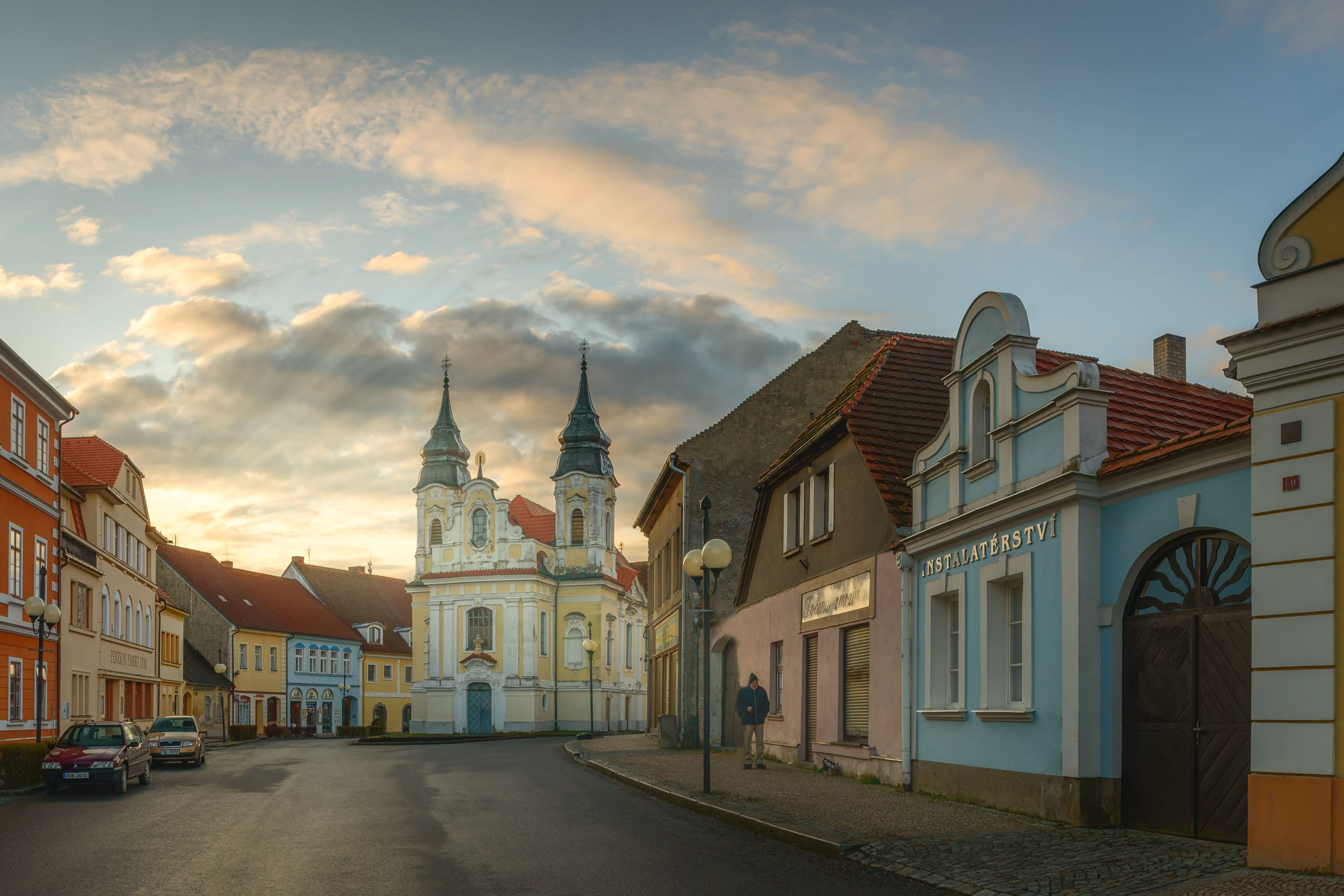 Uma rua de paralelepípedos ladeada por edifícios históricos, incluindo uma igreja com duas torres.