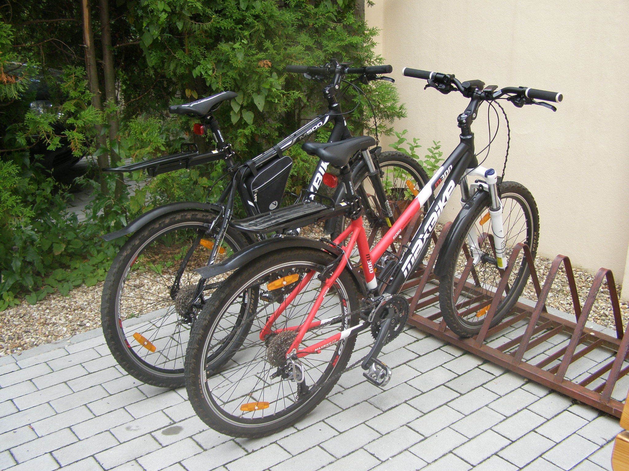 To cykler parkeret på en murstensbelagt overflade med et metalstativ.