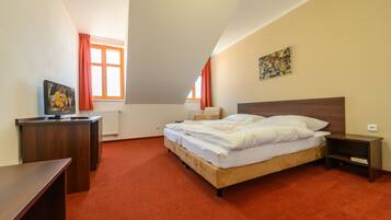 A bedroom with a bed, a desk, and a window with curtains.