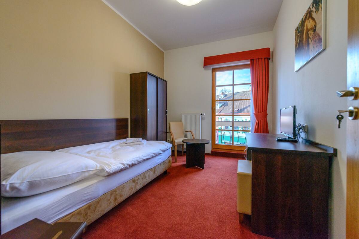 Ein Hotelzimmer mit Bett, Schreibtisch, Stuhl, Kleiderschrank und einem fensterbepflanzten Fenster.