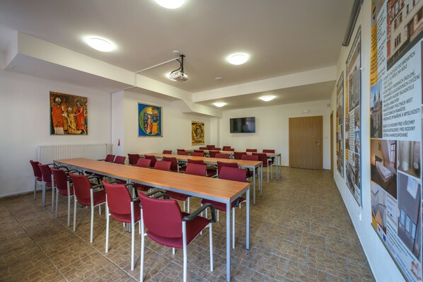 A conference room with a long table, red chairs, a projector, and informational posters on the walls.