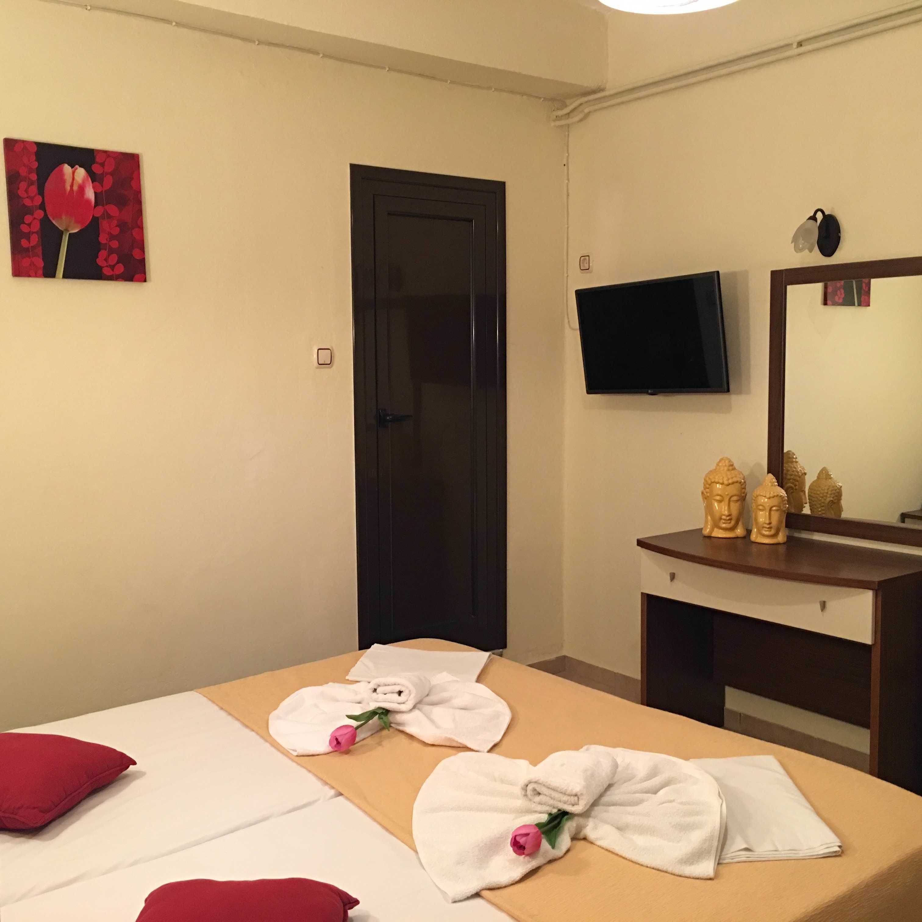 Habitación de hotel con cama, televisión, escritorio y estatuillas de Buda, además de un cuadro de un melocotón.