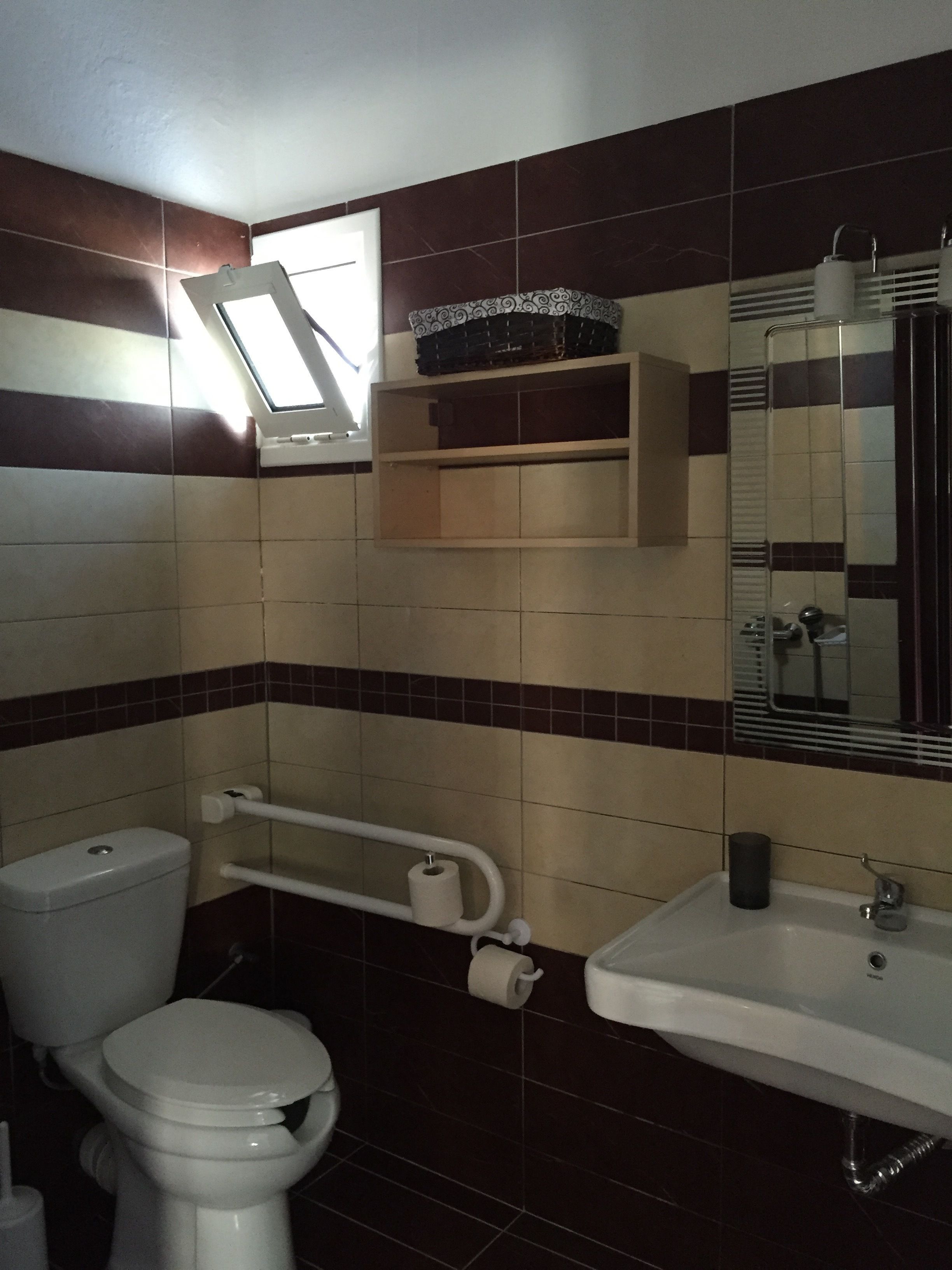 Un baño con inodoro, lavabo, espejo, ventana y un perchero para toallas.