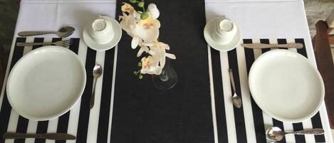 Una mesa dispuesta con platos blancos, cubiertos y un mantel con rayas negras y blancas.