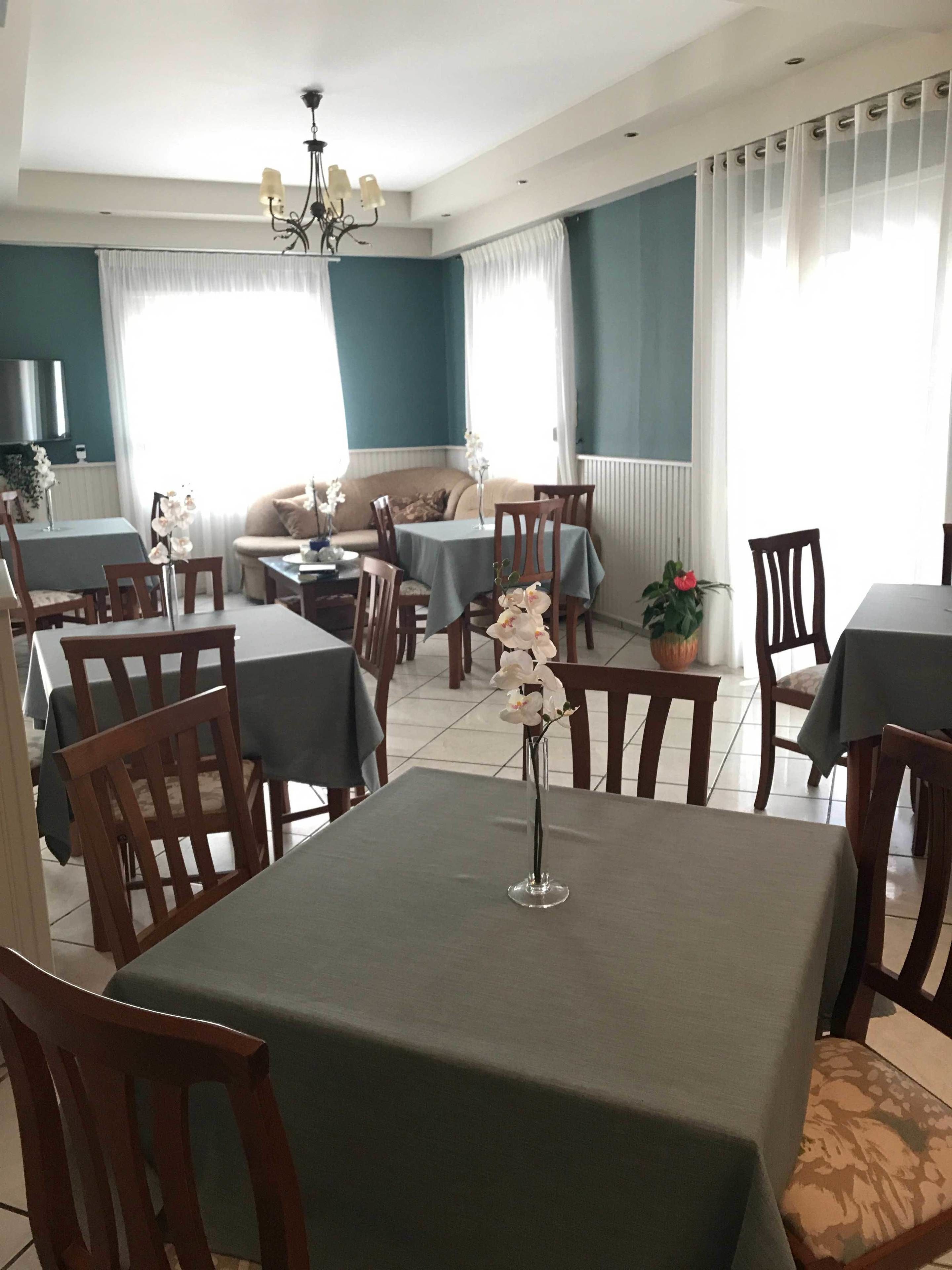 Un comedor con mesas y sillas, una araña y un sofá al fondo.