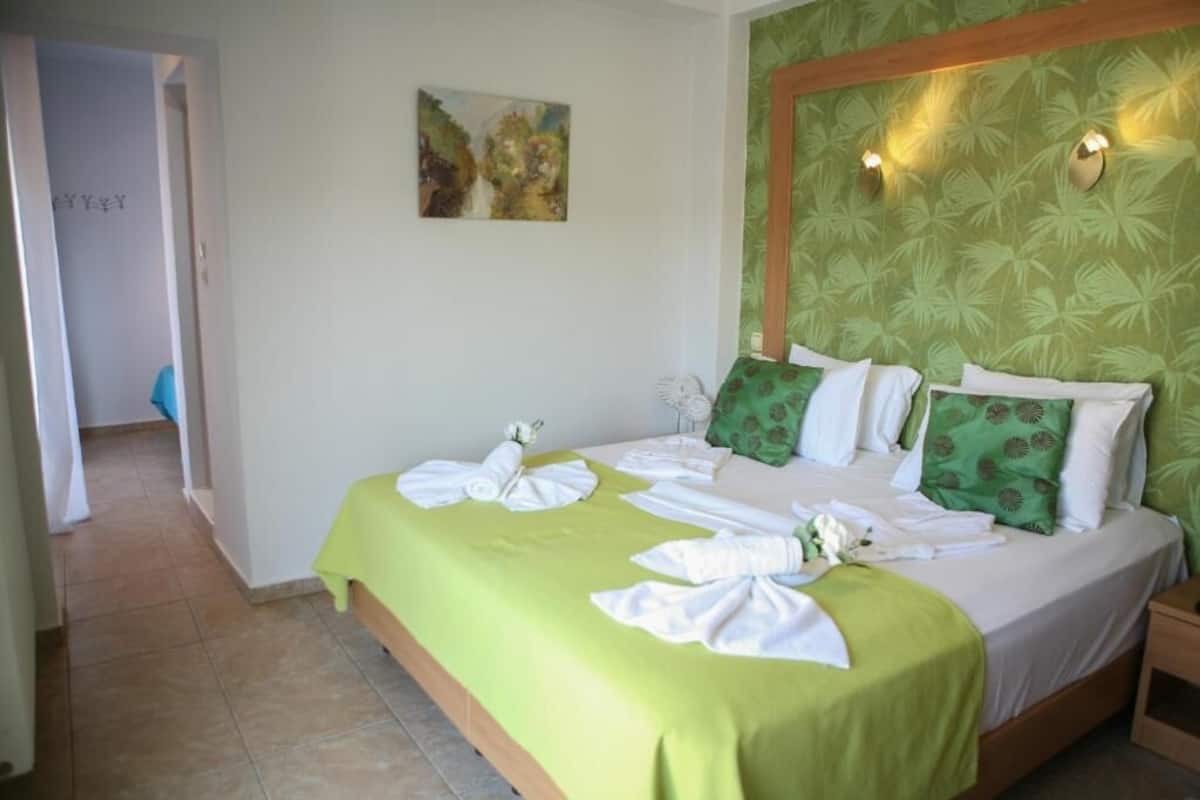 A hotel room with a bed, green bedspread, white towels, and a painting on the wall.