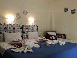 A neatly made bed with a blue bedspread, white pillows, and a decorative pillow with a nautical theme. There are two wall-mounted light fixtures above the bed, and a small decorative item on the nightstand.