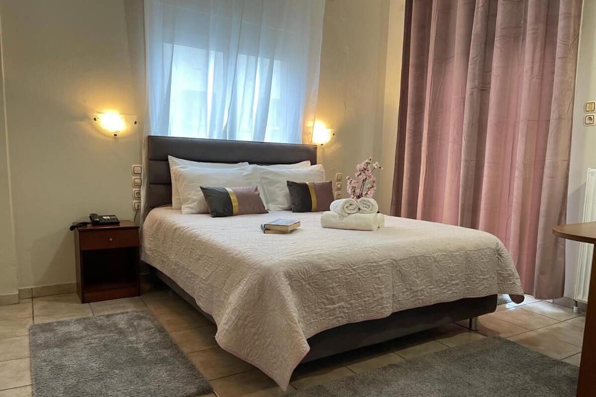 A neatly made bed with a white bedspread, a bedside table with a lamp, and a window with sheer curtains.