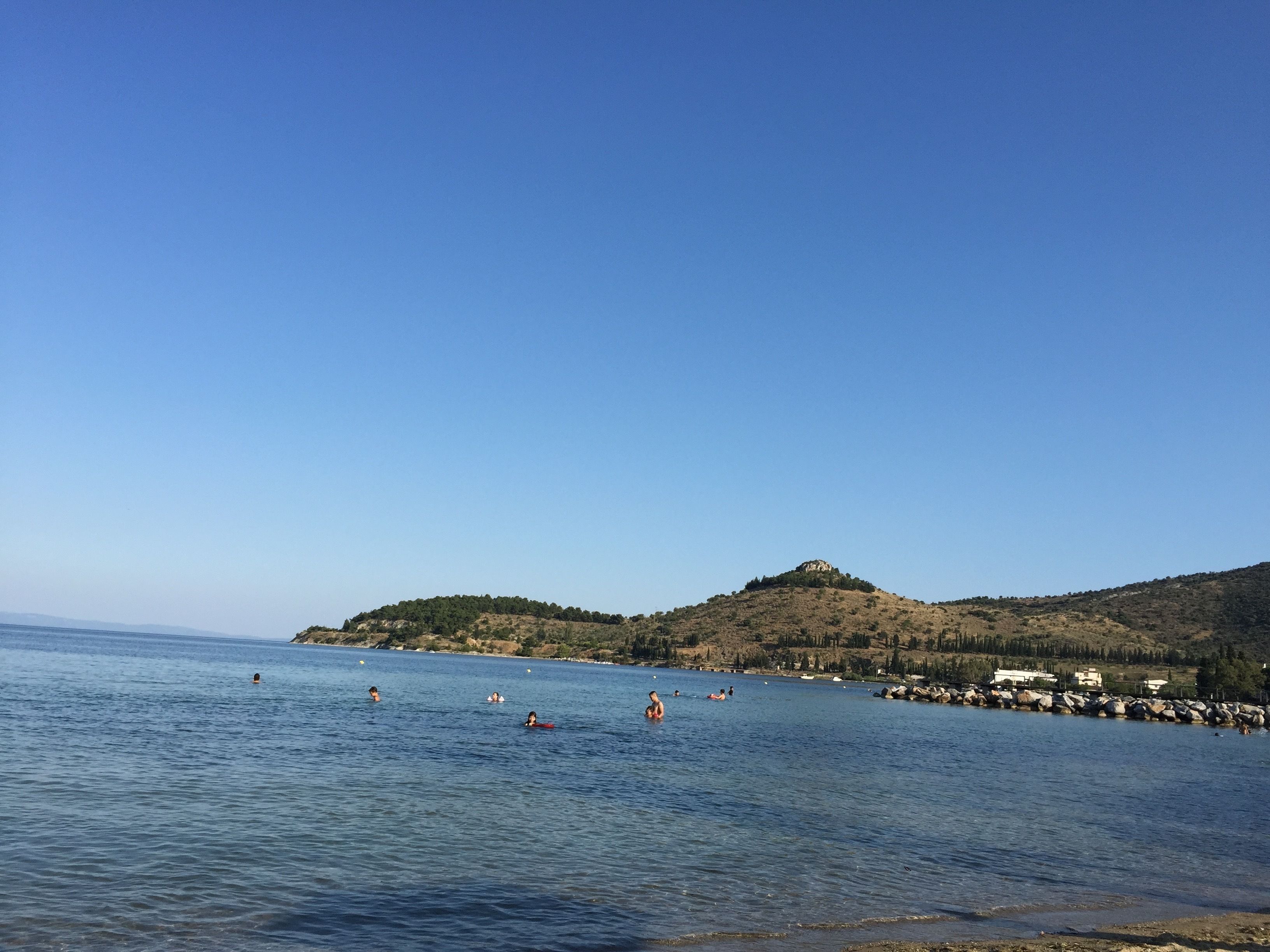 A coastal scene with clear skies, calm water, and a hilly landscape in the background.