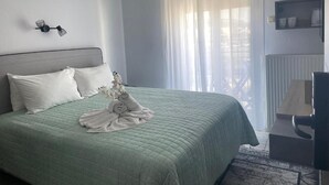 Ein ordentlich bezogenes Bett mit einem grünen Überwurf und weißen Kissen, ein kleiner Tisch mit einer Lampe und ein Topf mit einer Orchidee auf der Fensterbank.