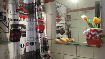 Un baño con cortina de ducha temática de Londres, un lavabo, un espejo y una repisa de cristal con un jarrón de tulipanes.