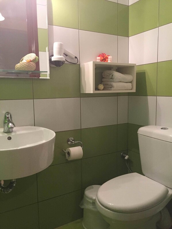 A bathroom with green and white tiles, a sink, a toilet, a towel rack, and a hairdryer.