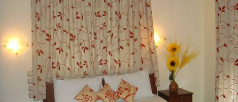 Una cama bien hecha con ropa de cama blanca y naranja, un florero con girasoles, y una lámpara fijada a la pared.