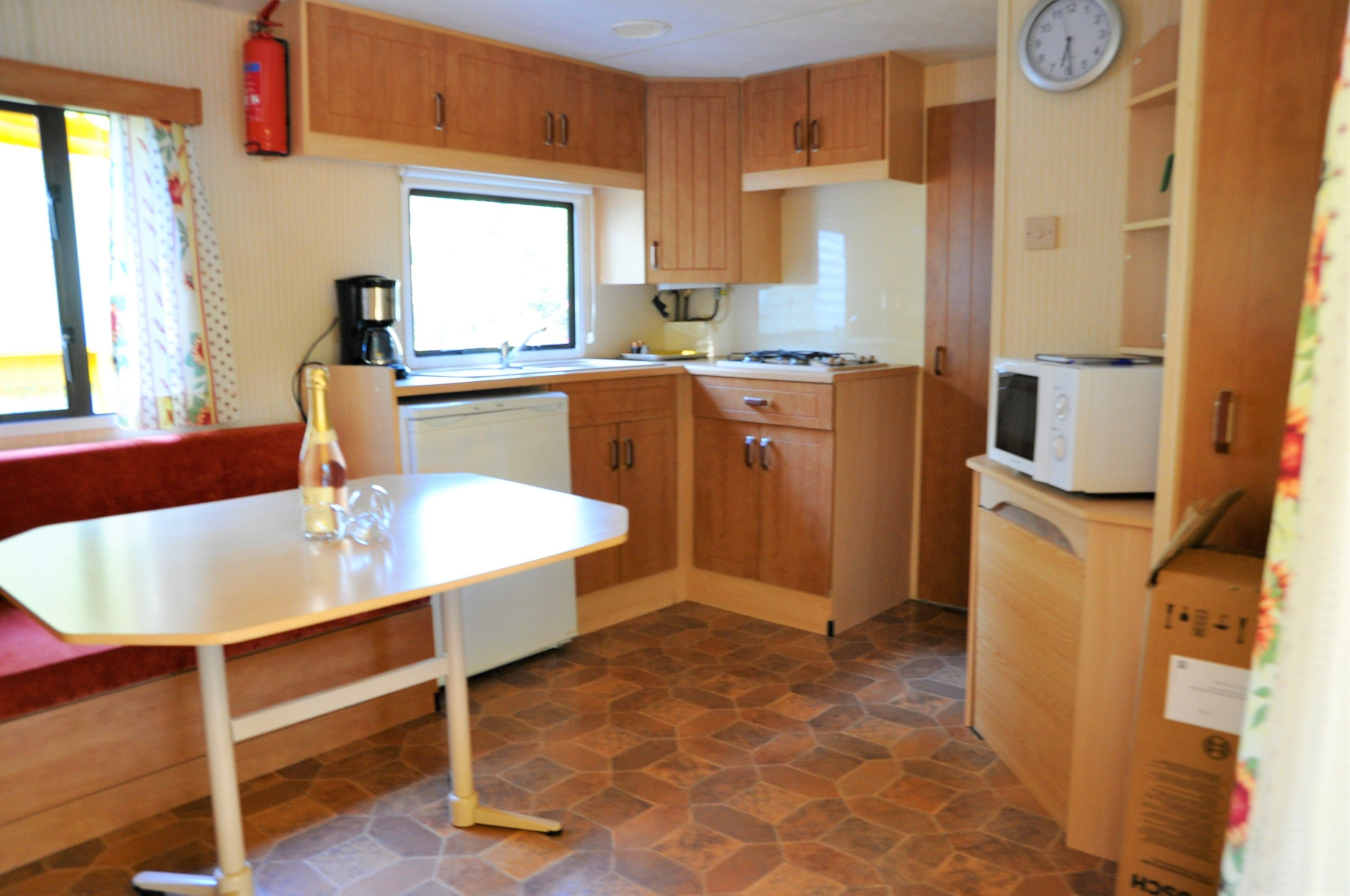 A compact kitchen with wooden cabinets, a white countertop, a stove, a microwave, and a clock on the wall.