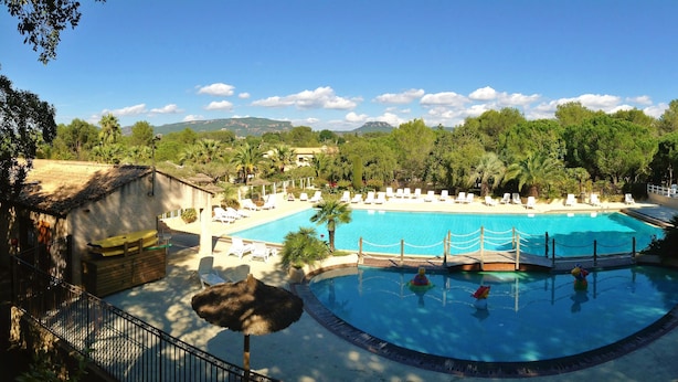 A resort with a large swimming pool surrounded by lounge chairs and umbrellas, set against a backdrop of trees and mountains. - Camping Lei Suves- Greenchalets (Roquebrune-sur-Argens)