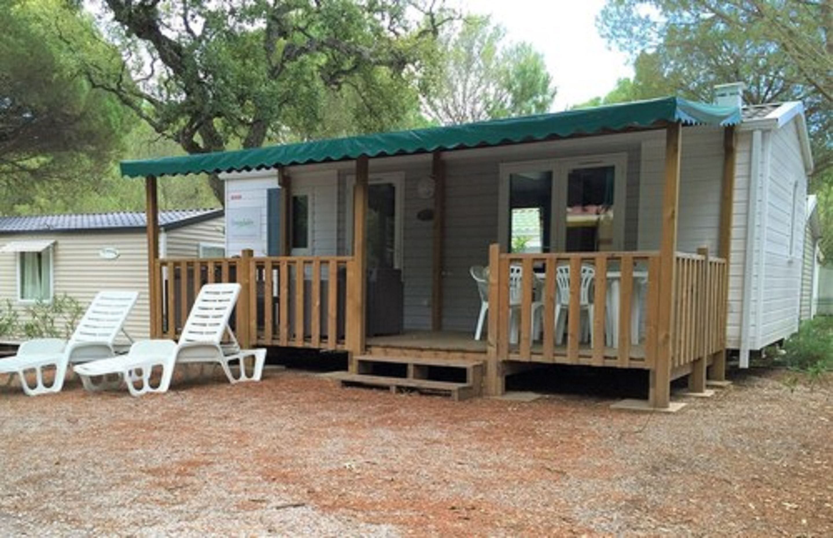 A small cabin with a porch, two white lounge chairs, and a gravel ground.