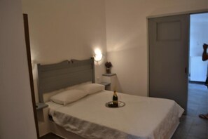 Un dormitorio con una cama, una mesita de noche con una botella y una lámpara de pared.