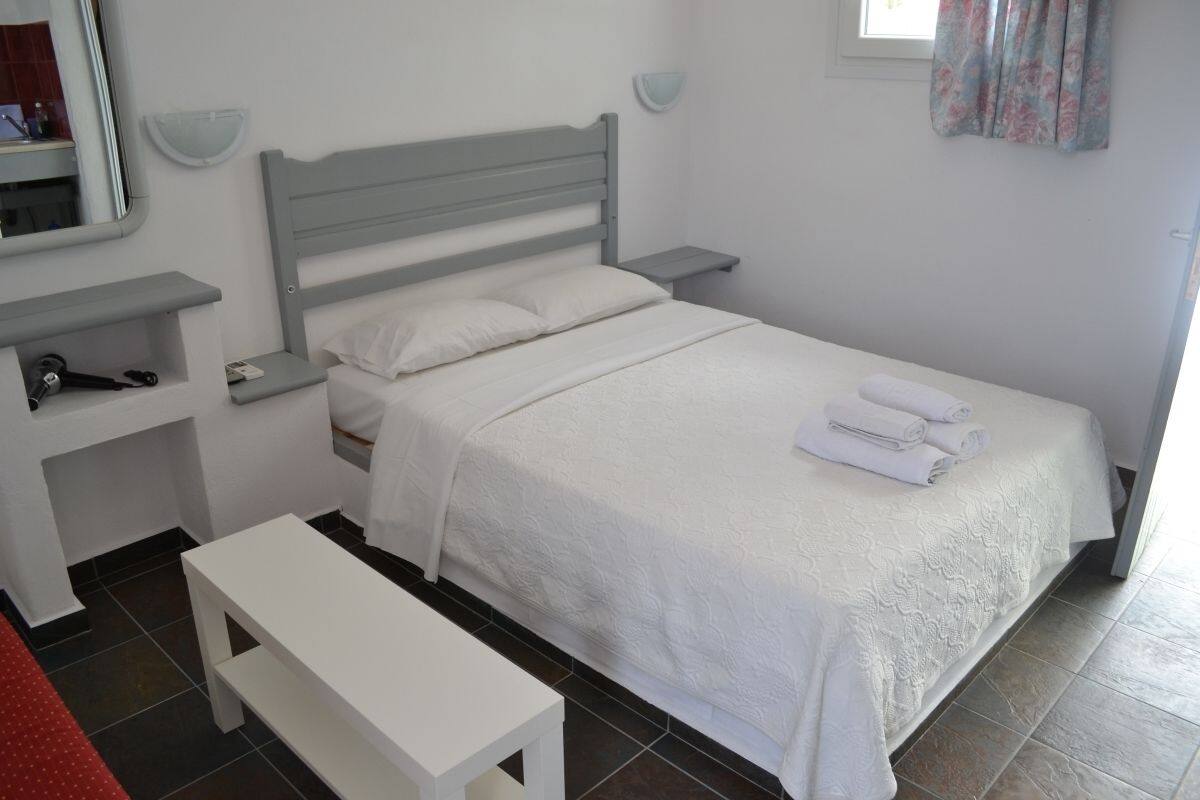 Un dormitorio ordenado con cama, mesitas de noche, un banco y un espejo.
