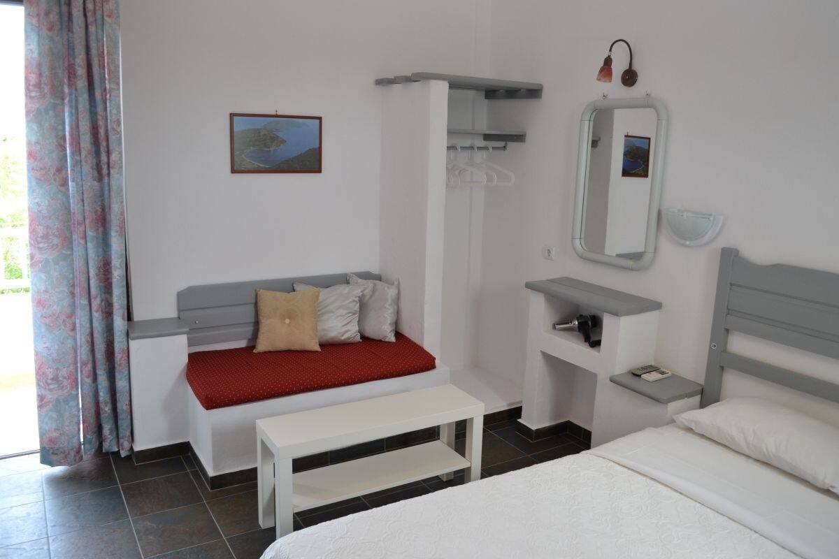 Un dormitorio con cama, un banco, una mesita de noche, un espejo y un estante en la pared.
