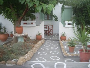 Un patio con plantas en macetas, un camino de piedra y una mesa con sillas preparadas para comer al aire libre.