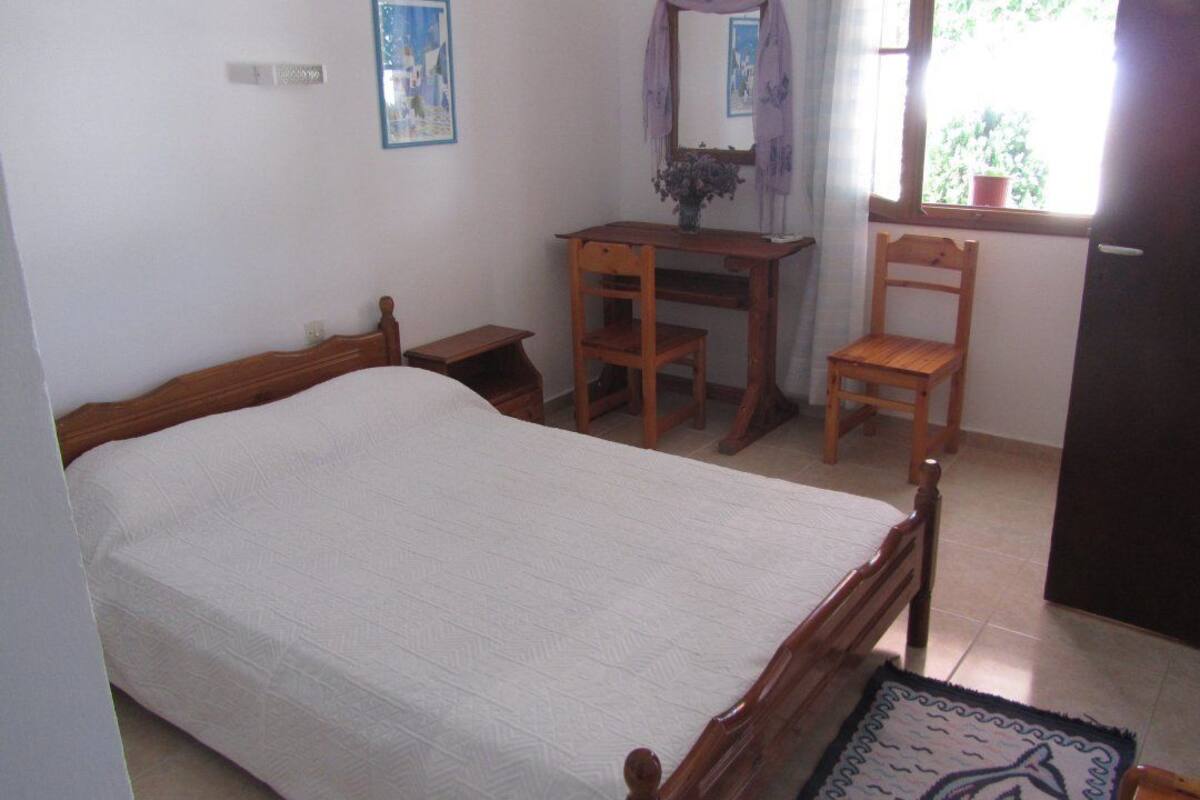 Un dormitorio con cama de madera, escritorio con silla, espejo y ventana con vista a follaje.