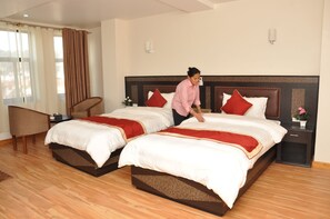 Habitación de hotel con dos camas, una silla, una mesita de noche y una ventana con cortinas.