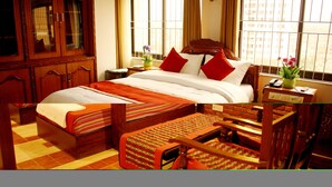 A neatly arranged hotel room with a large bed, a wooden wardrobe, a bedside table with a lamp, and a window with a city view. - Mandala Hotel Pvt.Ltd. (Kathmandu)
