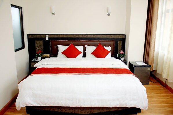 A neatly made bed with a red and white bedspread, a wooden headboard, and a small bedside table with a lamp. - Mandala Hotel Pvt.Ltd. (Kathmandu)
