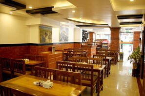 A restaurant with wooden tables and chairs, a brick accent wall, and paintings on the walls. - Mandala Hotel Pvt.Ltd. (Kathmandu)