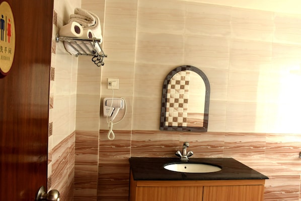 Un baño con pared de mármol, un lavabo con encimera negra, un perchero, un teléfono y un espejo con marco a cuadros.